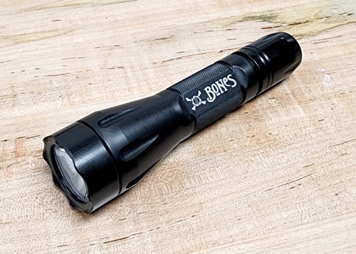 Picture showing a Black Elzetta Bones Flashlight on a wooden surface.