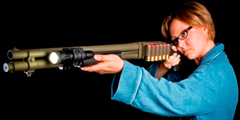 Woman in bathrobe aiming shotgun with ZSM mount and Elzetta flashlight.