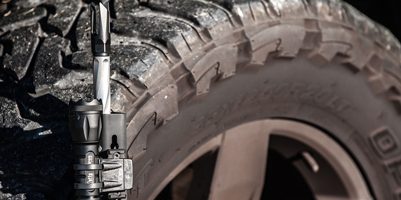 Closeup of Truck Tire with Rifle Leaning against it with Elzetta Bravo Flashlight Mounted on it with ZRX Flashlight Mount